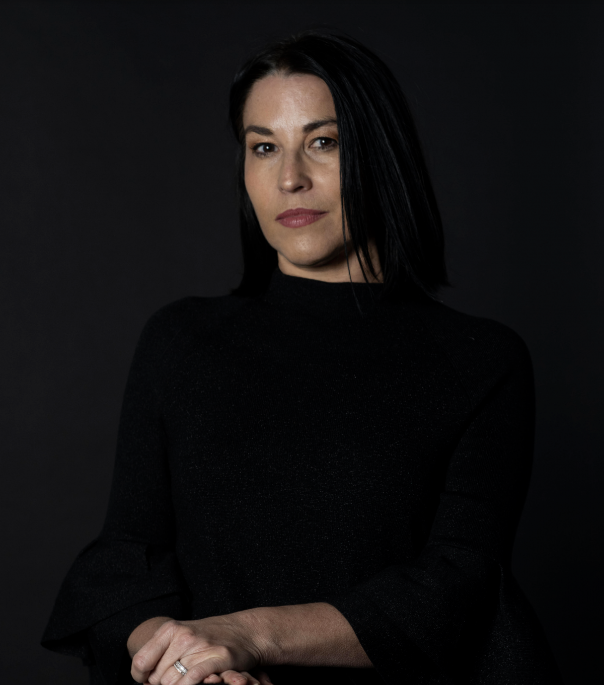 Headshot of Arlene Davila, wearing black and dark gray background