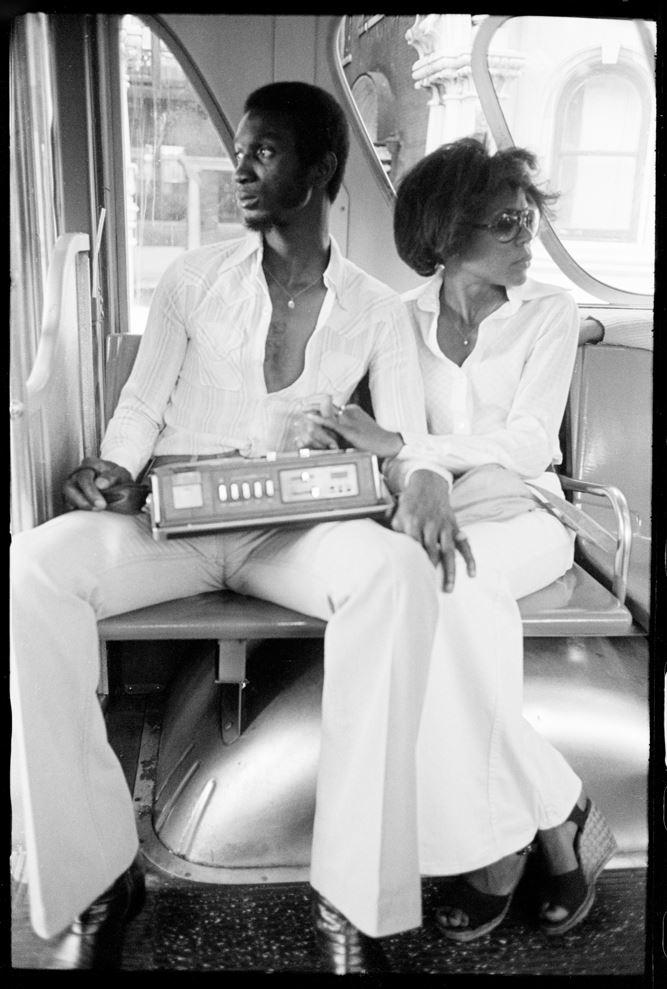 Black and white photo of a man and woman from the 60s on a bus holding a radio