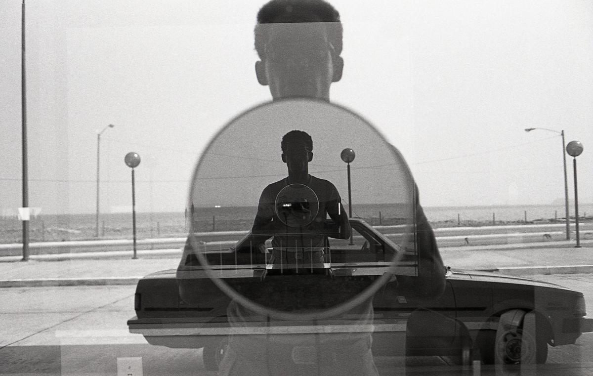 Black and white photograph of a man taking a photograph in a window with a reflection