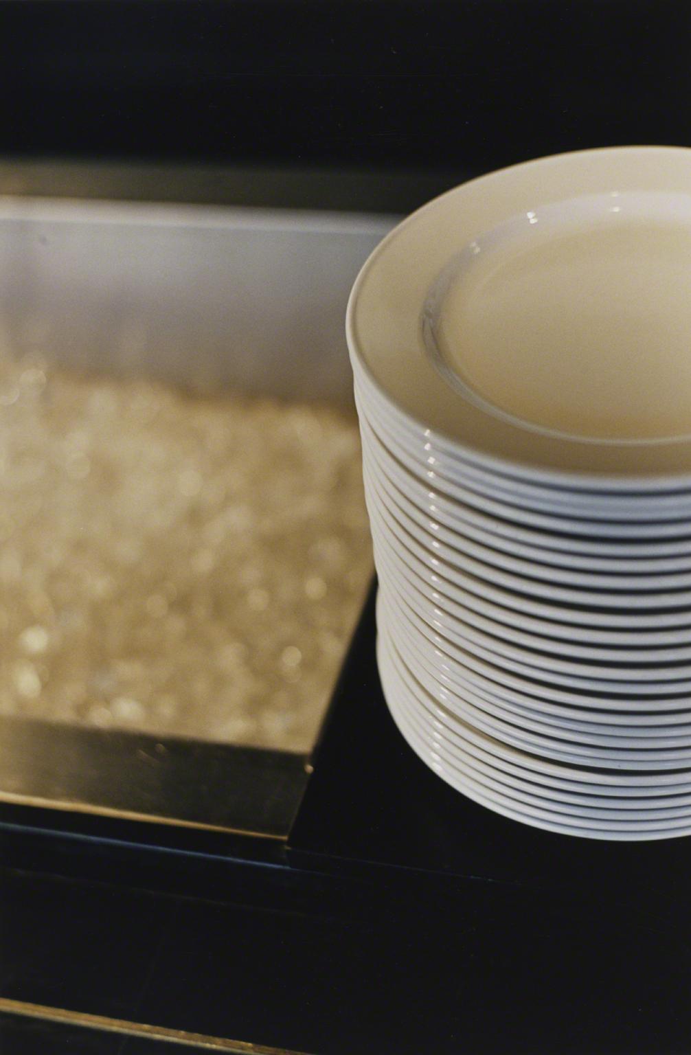 Color photograph of a stack of white plates on a counter next to a basin