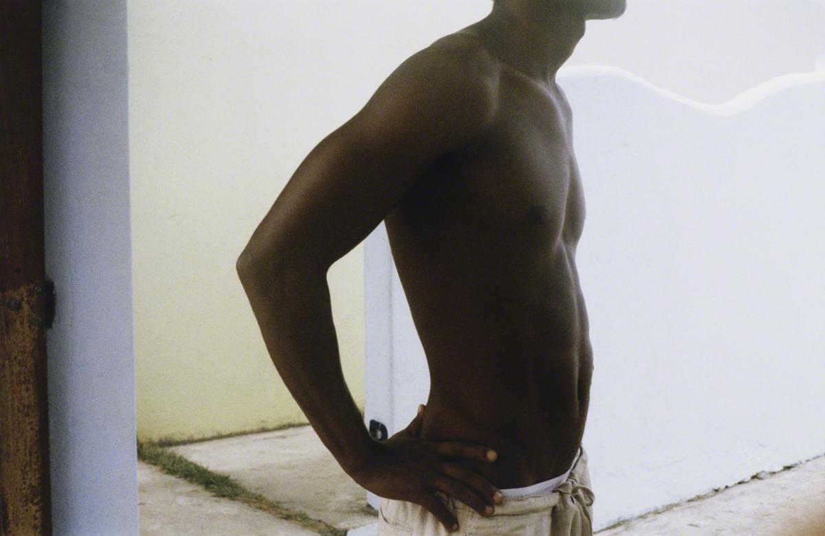 Color photograph on a shirtless black man in profile with head cropped off and hands on hips