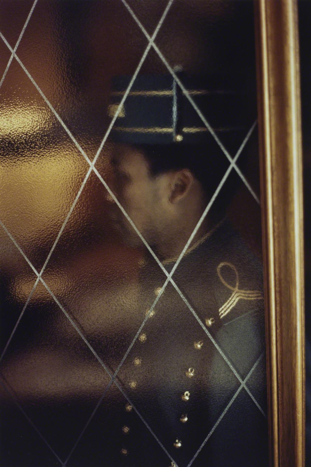Color portrait of a valet or doorman that is partially obscured by dimpled glass 