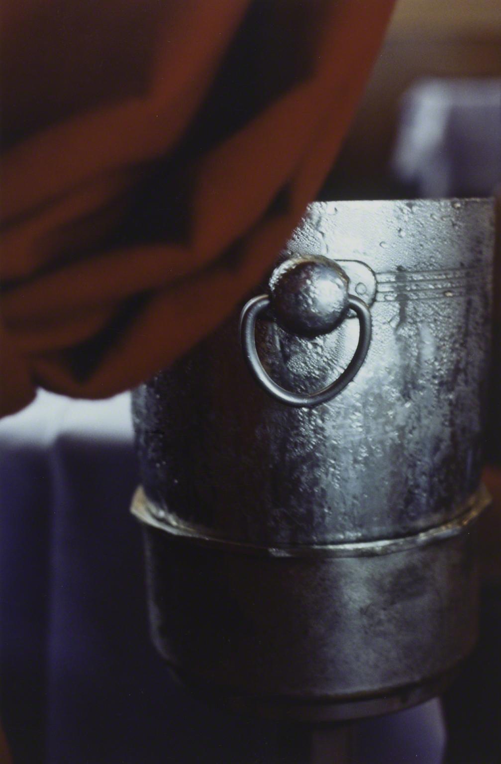 Color photograph of a steel ice bucket with condensation set slightly behind a red curtain 