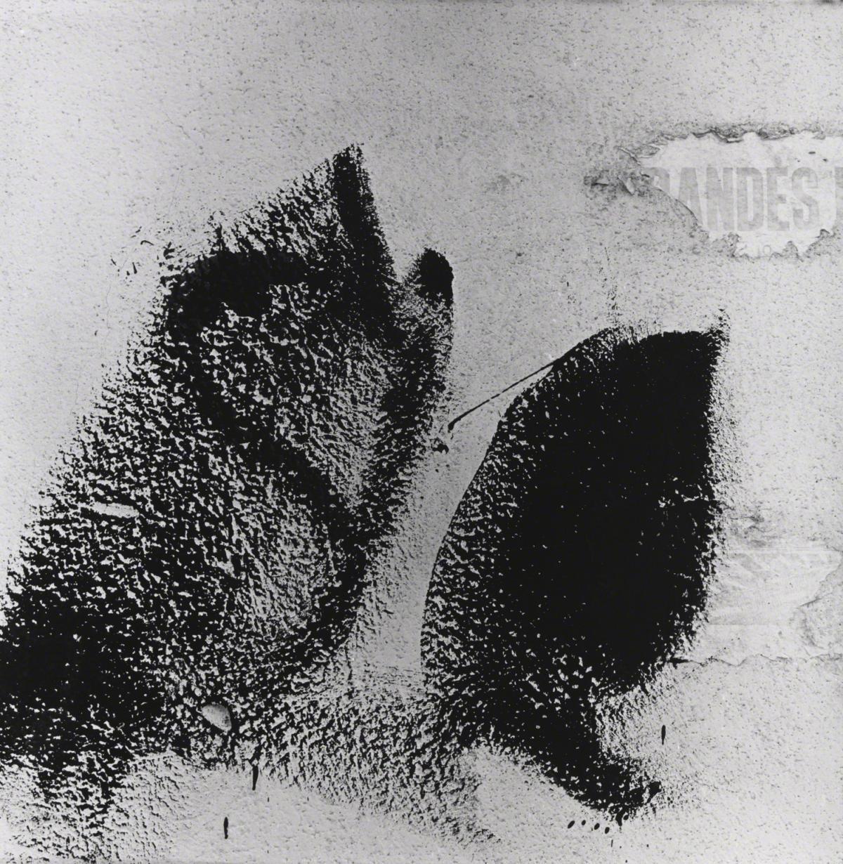 Black and white photograph showing smears of back paint on a white wall with remnants of torn posters