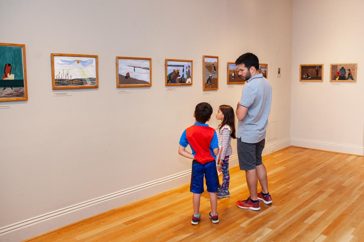Man and two kids looking at art on the walls in a gallery