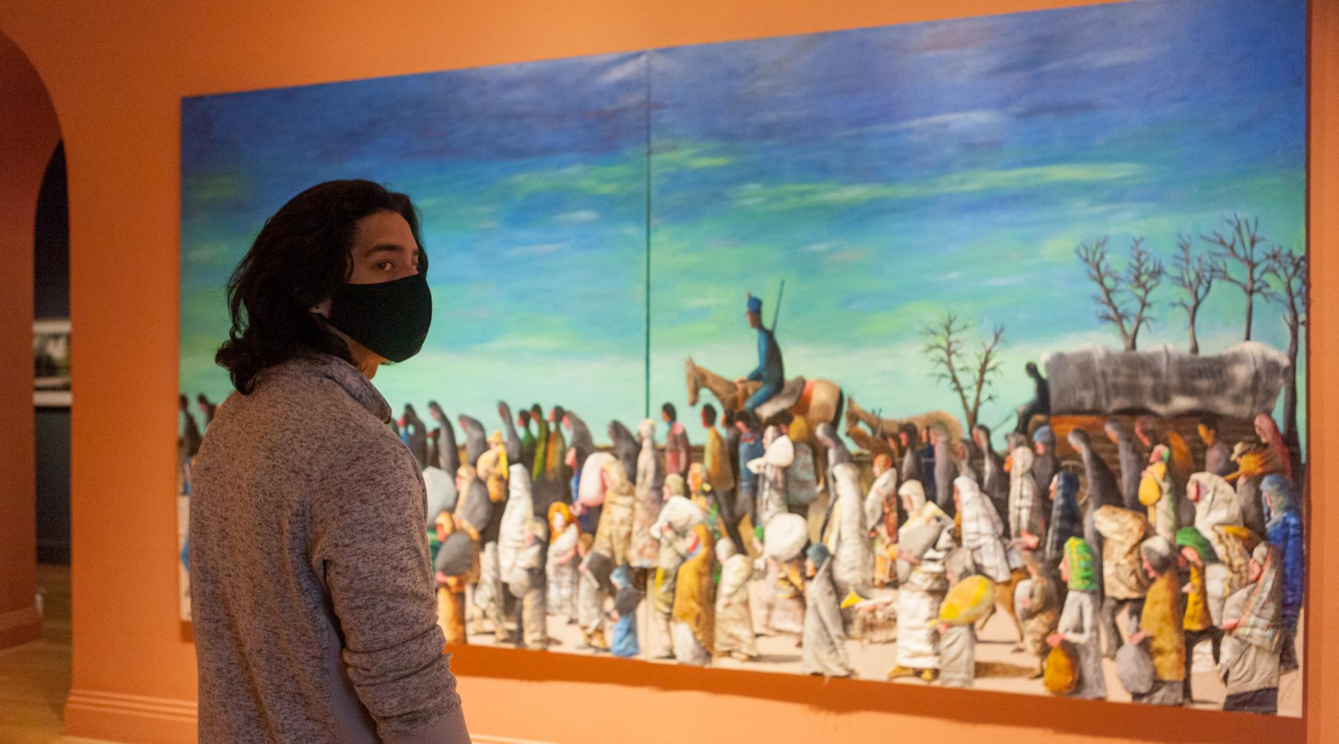 Photo of a person standing in front of Benny Andrews's painting "Trail of Tears" and looking to the right