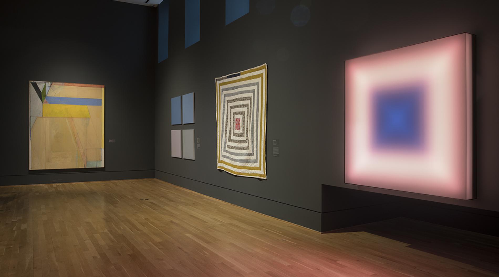Photograph of four colorful artworks in a museum gallery with dark blue walls