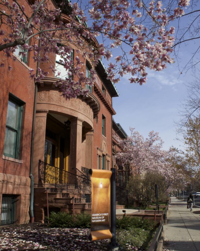 Photograph of the Phillips House with a yellow banner in front and cherry blossoms