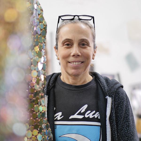 Photo portrait of Alyson Shotz smiling, with shimmering artwork in front of her