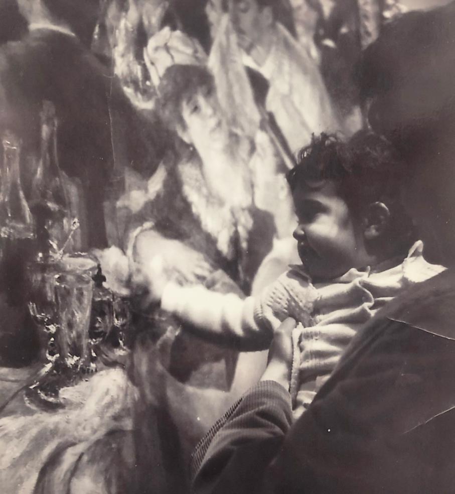 Old black and white photo of someone holding a baby that is reaching out to touch Renoir's Luncheon of the Boating Party