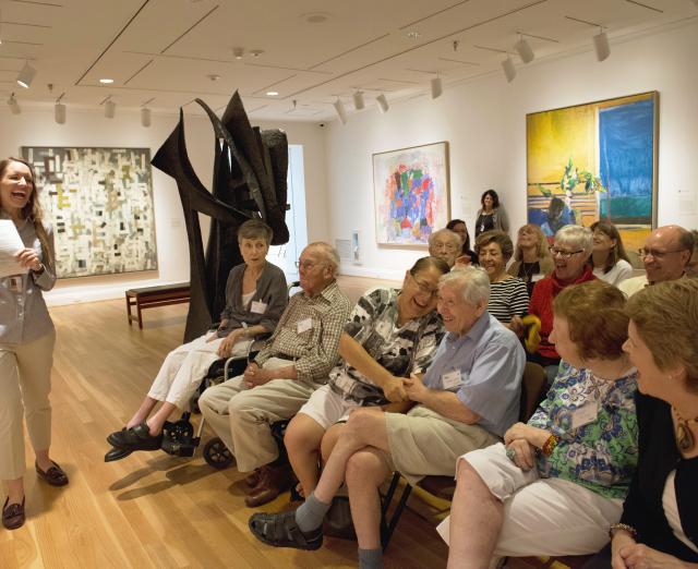 Photograph of woman giving a talk to older adults in a gallery with artwork