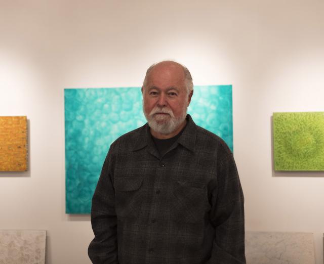 Photograph of Robin Rose with his artwork on the walls behind him