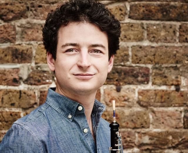 Man with oboe in front of brick wall