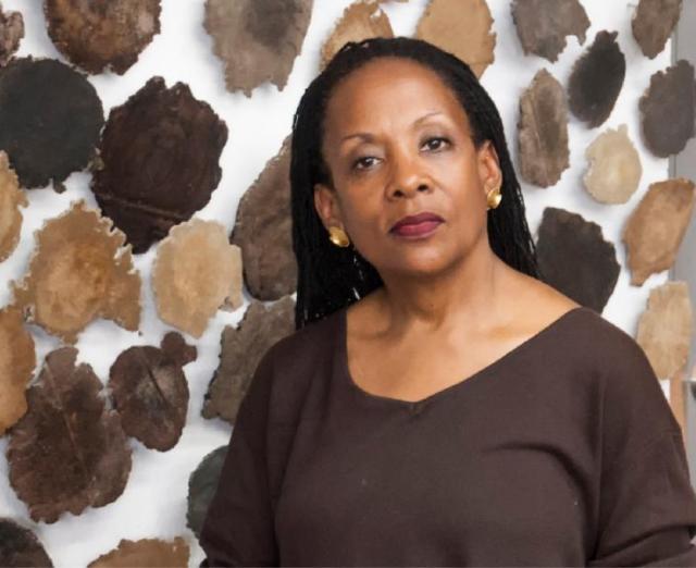 Headshot of a woman standing in front of a lot of brown circular artwork on the wall