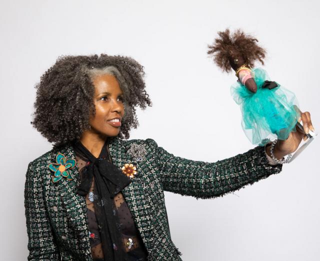 Photo of Sherri Lumpkins holding up and smiling at a Black baby doll
