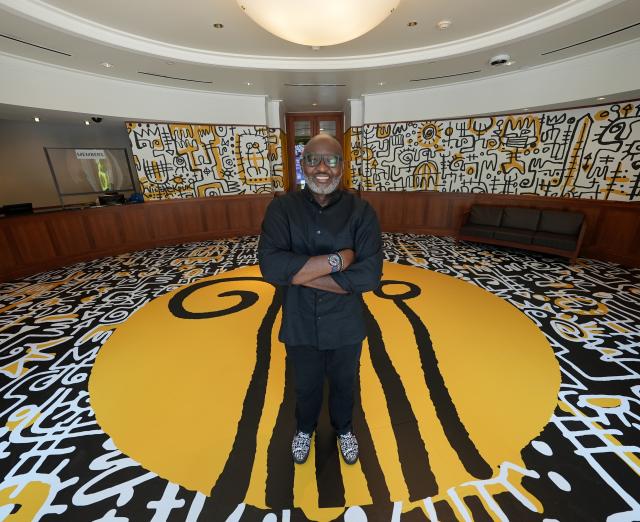 Photo of Victor Ekpuk standing in a large circular room covered in his artwork