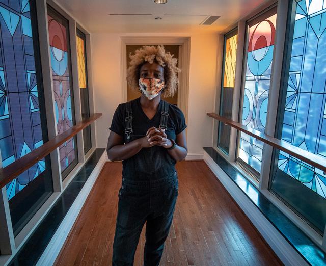 Photo of Nekisha Durrett standing in the Phillips bridge with her stained-glass inspired artwork on the windows