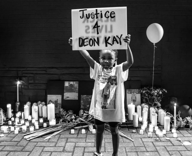 A black and white photo of a little girl holding up a sign that says Justice 4 Deon Kay