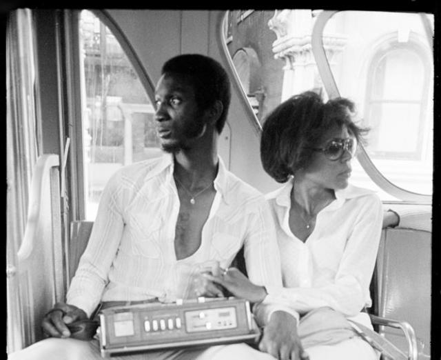 Black and white photo of a man and woman from the 60s on a bus holding a radio