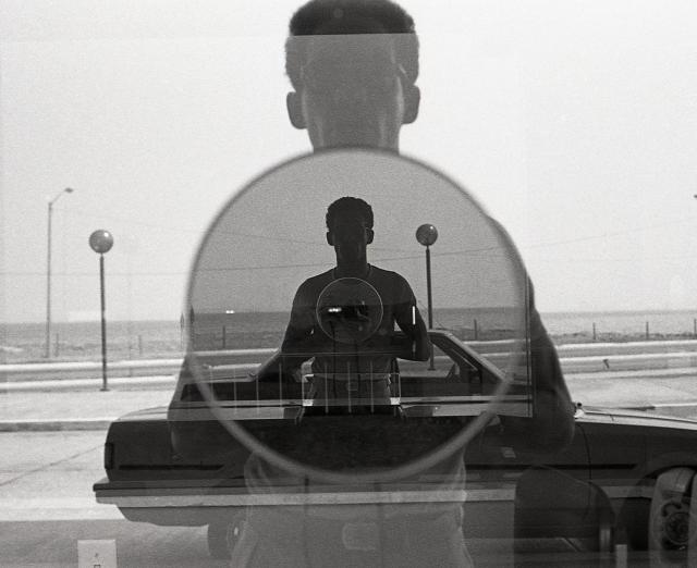 Black and white photograph of a man taking a photograph in a window with a reflection