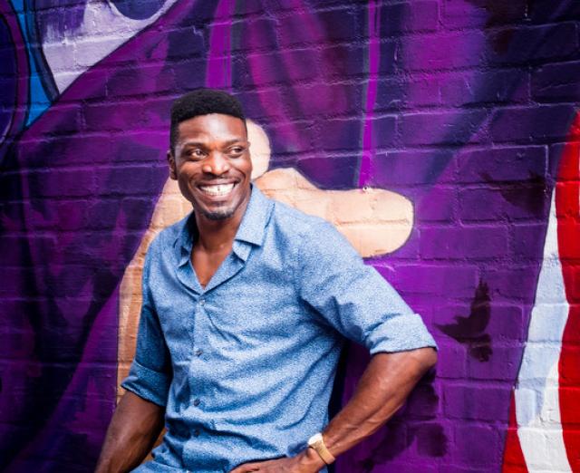 Photograph of Anieka Udofia smiling and standing against a purple wall