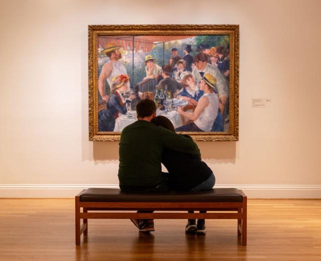 Two people embracing on a bench looking at Renoir's Luncheon of the Boating Party