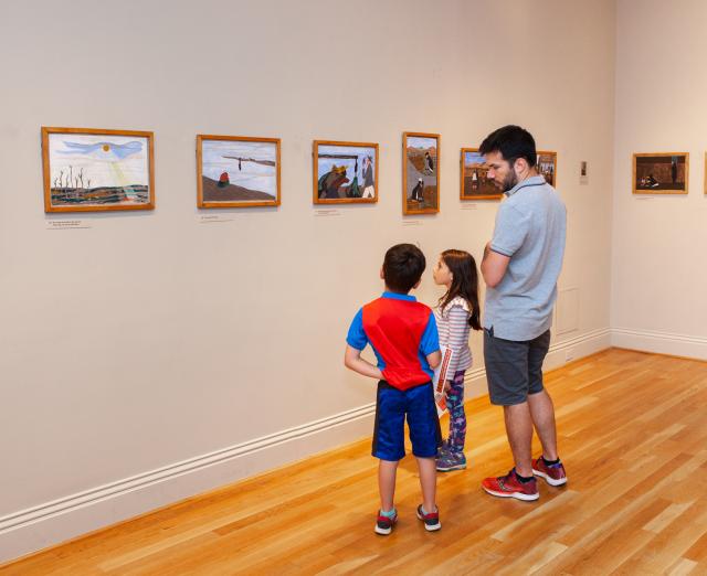Man and two kids looking at art on the walls in a gallery