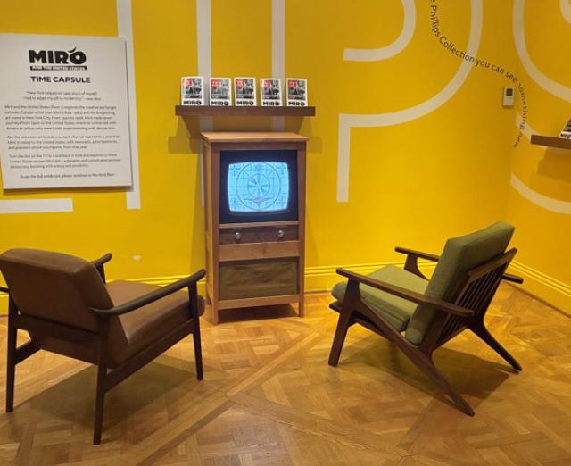 Two chairs in front of a retro tv against a yellow wall 