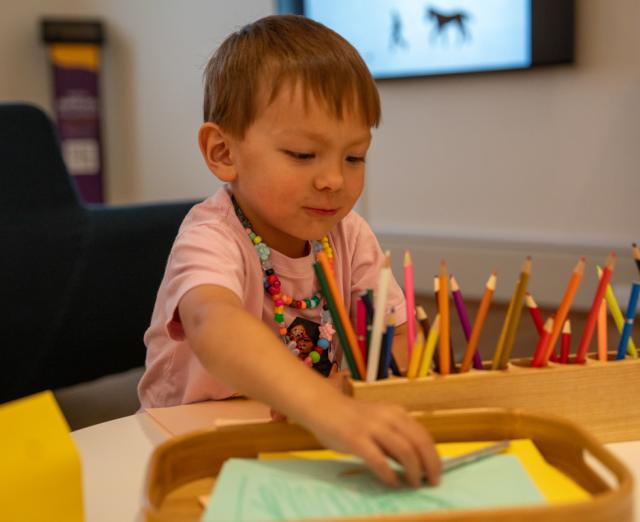 A kid sitting at a table with paper and color pencils