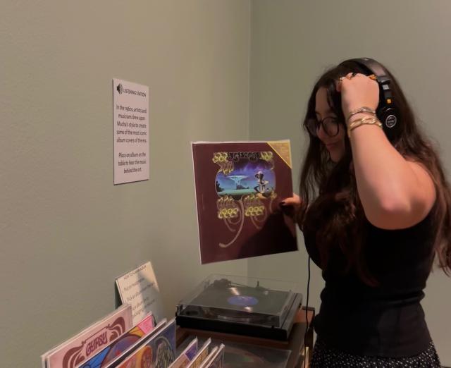 Someone standing by a record player and records listening with headphones on