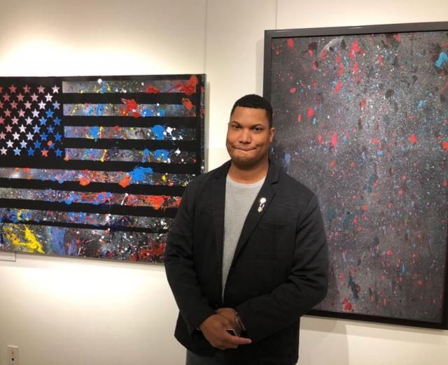 Photo of Zach Herrick with two pieces of artwork created through American Heroes HeART