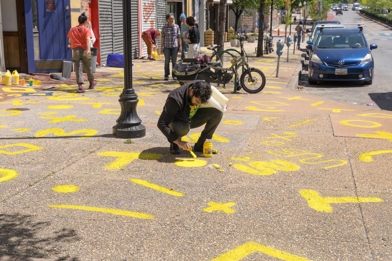 Image of artist painting on sidewalk with volunteers using symbols during the Asian North festival in Baltimore