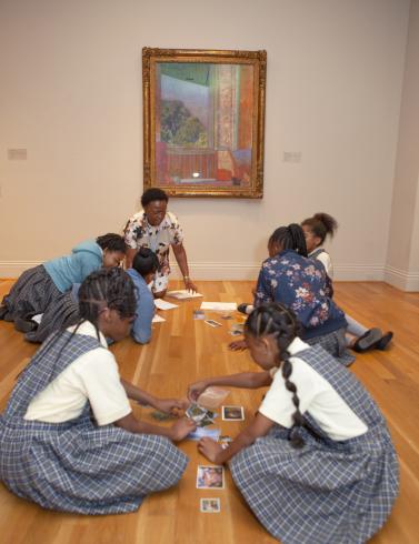 Photograph of students in gallery with an educator in front of a framed painting