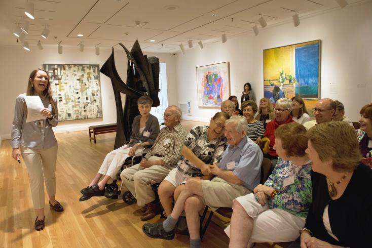 Photograph of woman giving a talk to older adults in a gallery with artwork