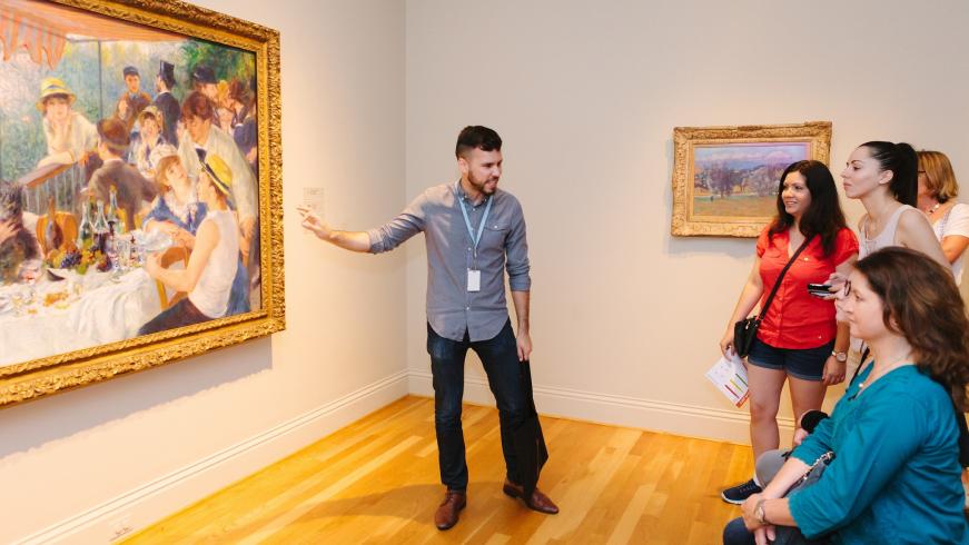 Man standing in front of four women, talking about a painting behind him that is he pointing to