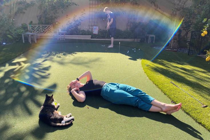 Photograph of a person laying on a lawn next to a cat