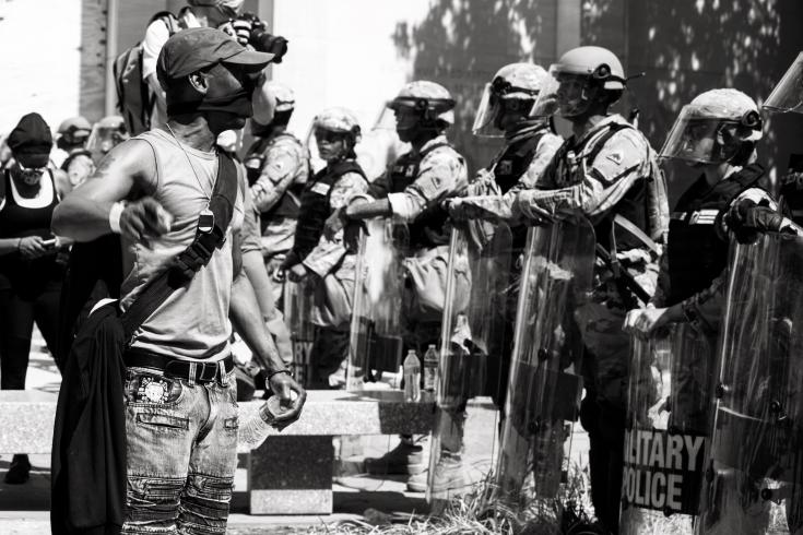 Black and white photograph of a protestor confronting armed police