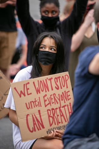 Photograph of a person holding a sign that says "We won't stop until everyone can breathe"