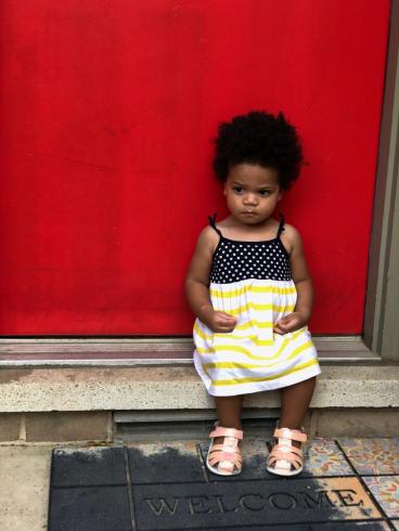 Photograph of young child in dress sitting in front of a red wall
