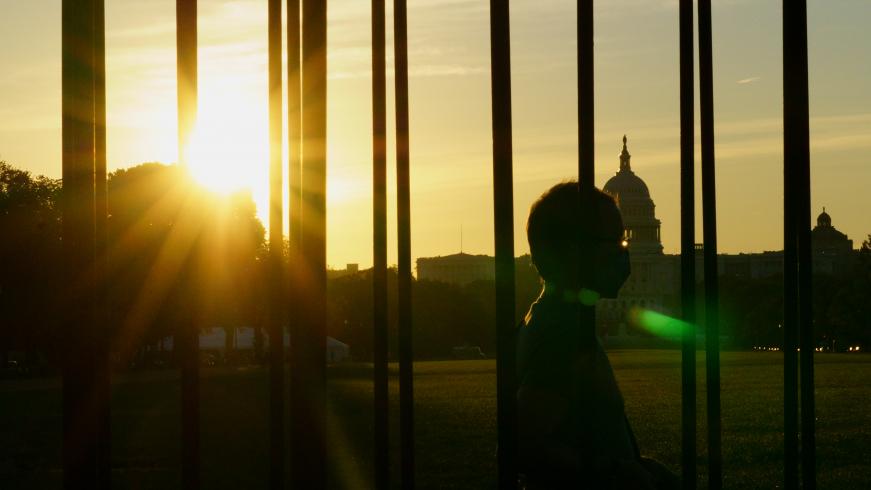 Photograph of a person walking by the Capitol, backlit by the sun