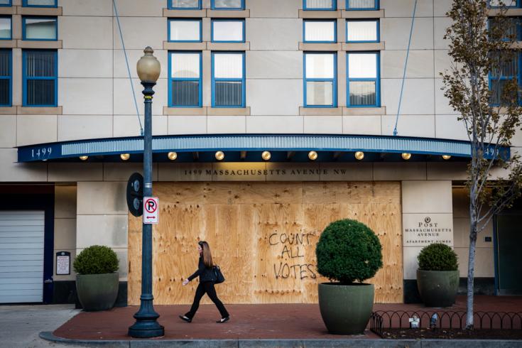 Photograph of a woman walking in front of a boarded up building