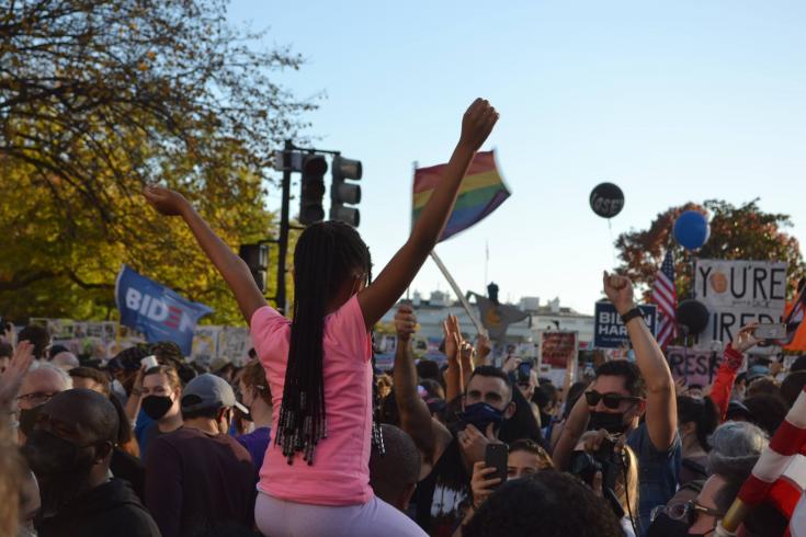 Photograph of a young girl on someone's shoulders in a cheering crowd outside