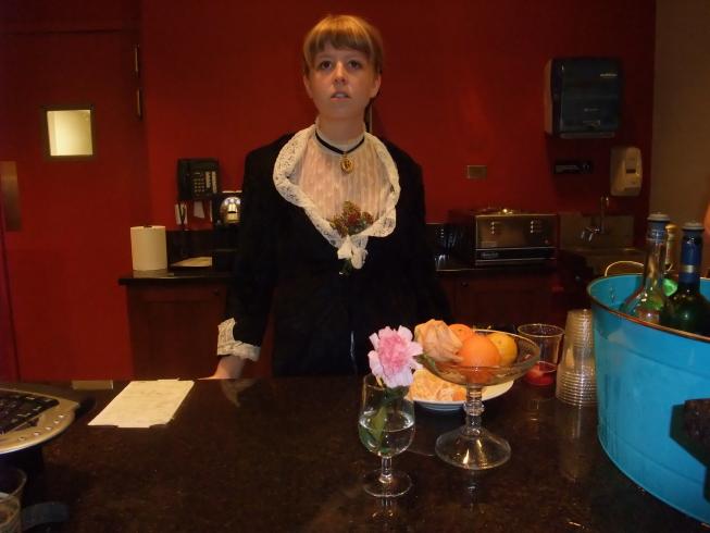 A young woman bartender stands at attention with a bouquet of flowers tucked down her blouse.