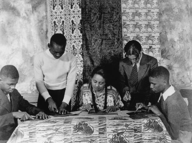 black and white photograph of 5 people gathered around table making prints