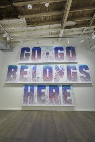 Photograph of the words "Go-Go Belongs Here" in all caps in purple letters on a white wall