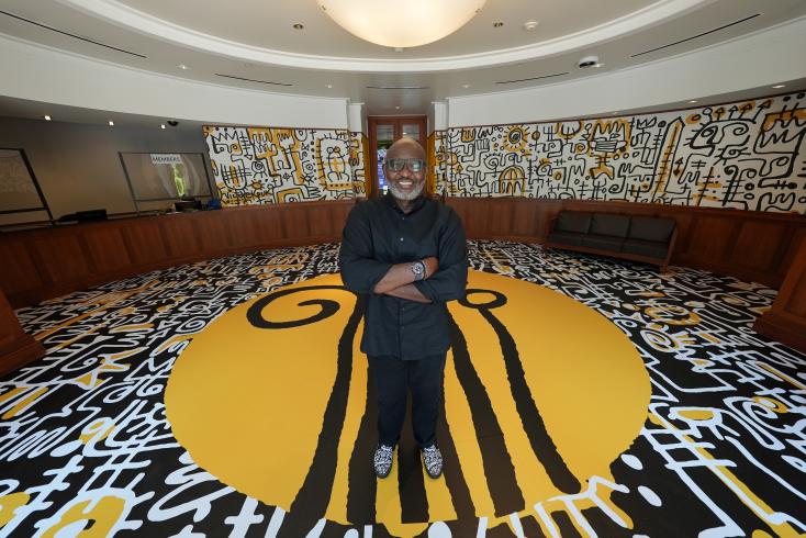 Photo of Victor Ekpuk standing in a large circular room covered in his artwork