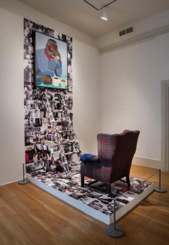 Photograph of an artwork with an armchair facing a ladder with a portrait of Jacob Lawrence at the top