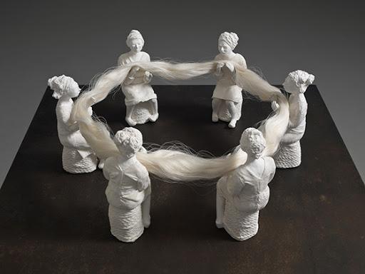 6 women seated in circle, holding a circle of silk, all in white