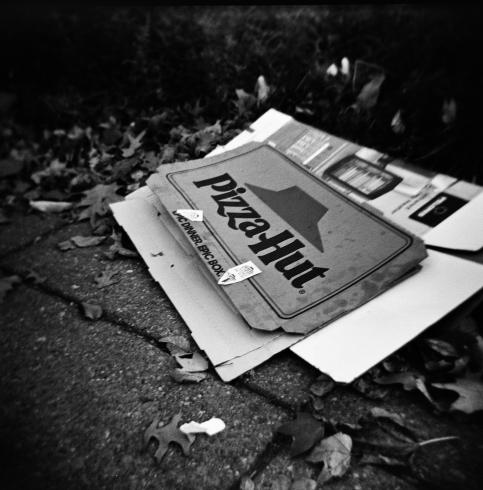 Black and whit image of a crumpled pizza box laying on the street