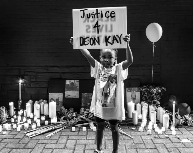 A black and white photo of a little girl holding up a sign that says Justice 4 Deon Kay